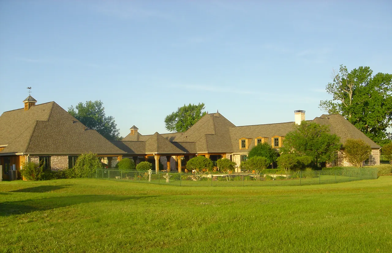 A long brick house in East Texas with tan shingle roofs, two cupolas and a green lawn in front, under a clear blue sky