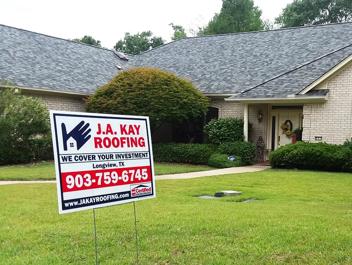 A J. A. Kay Roofing yard sign on a lawn in front of a brick house with a new gray shingle roof