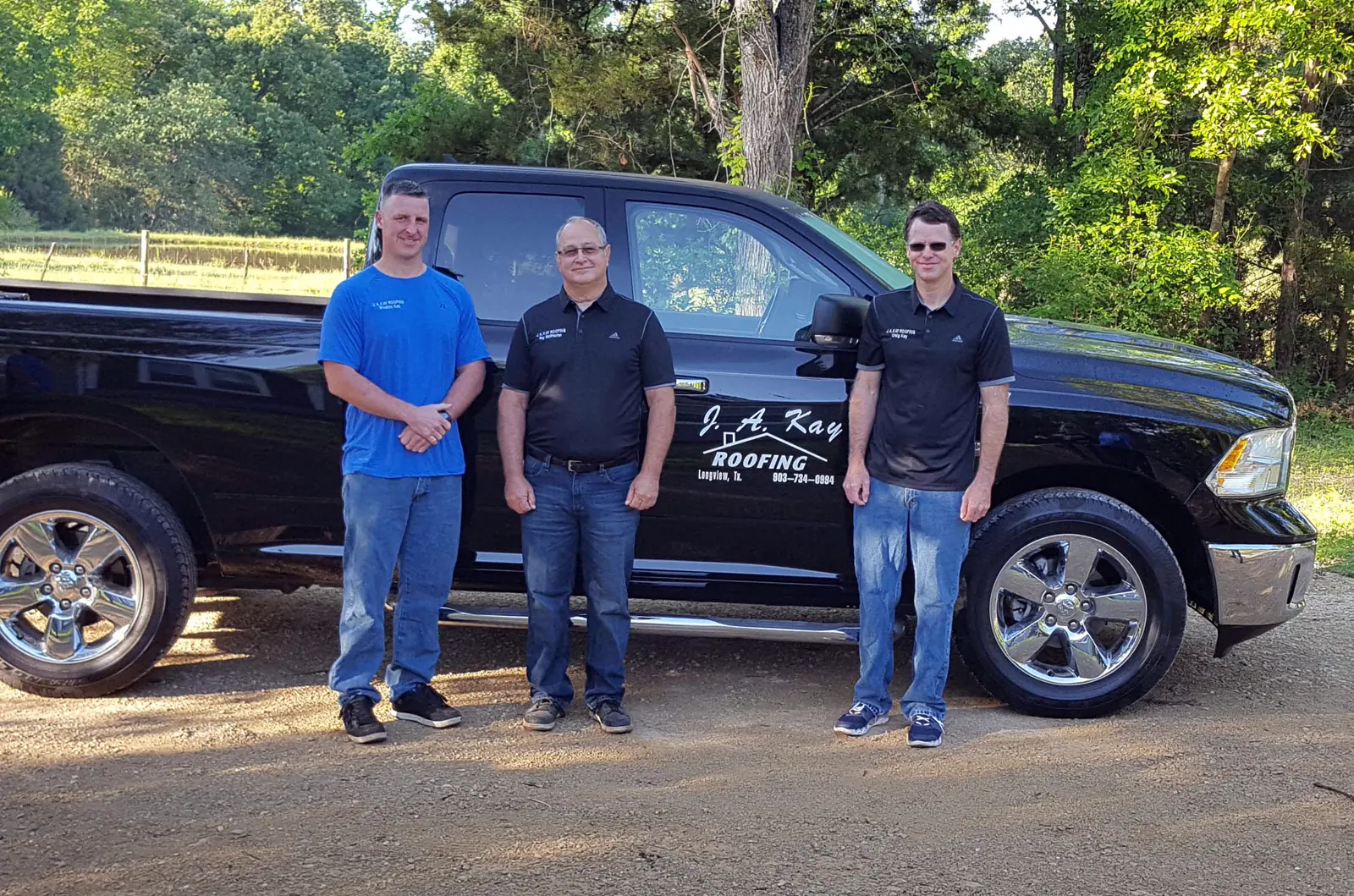 Three men standing in front of a black pickup truck lettered J. A. Kay Roofing